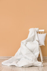 Fototapeta na wymiar Chair with white blanket and pillow near beige wall