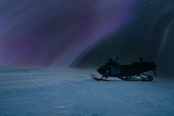 Nice night side photo of snowmobile stands at mountain under frosty winter sky with Northern Lights...