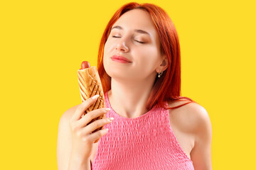 Beautiful young woman with tasty french hot dog on yellow background