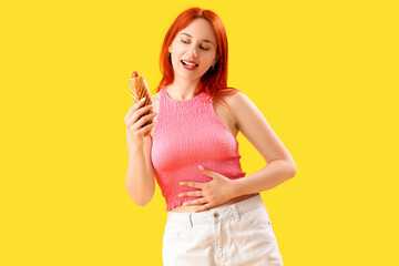 Beautiful young woman with tasty french hot dog on yellow background