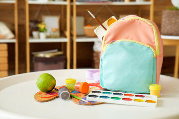School backpack and paints on table in room