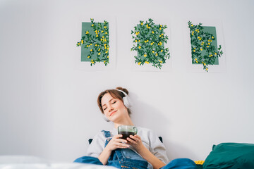 Woman with closed eyes listen music and enjoy cup of coffee or tea. Calm female spend free time at...