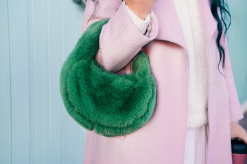Close up cropped stylish woman in pink coat holding bright green fluffy fur bag in her hands....