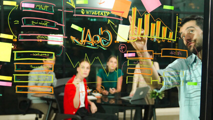 Young beautiful businesswoman point sticky notes at glass wall with business plan, strategy and walking back to meeting table while expert colleague brainstorming idea, solving problems. Tracery
