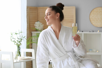 Beautiful young woman with glass of champagne in spa salon