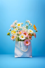A shopping bag full of beautiful colorful flowers on pastel blue background