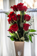bouquet of red roses in a vase by a window
