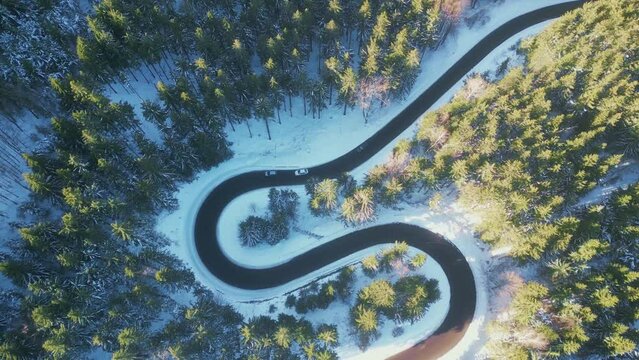 Twisted road in winter forest. Asphalt road serpentine and snowy landcape around. Aerial 4K footage from drone flight