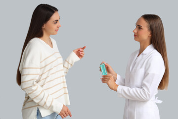 Female gynecologist with contraceptive pills and patient on light background