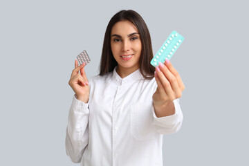 Female gynecologist with contraceptive pills on light background