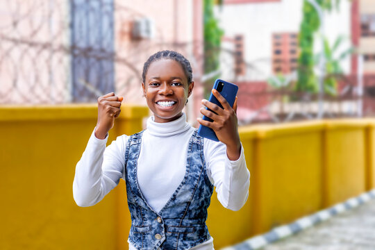 An excited young black Woman Multitasking while holding Cell Phone