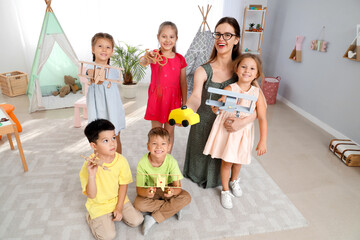Little children and nursery teacher with toys in kindergarten
