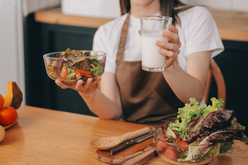 Delicious fruit and vegetables on a table and woman cooking. Housewife is cutting green cucumbers on a wooden board for making fresh salad in the kitchen.