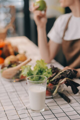 Delicious fruit and vegetables on a table and woman cooking. Housewife is cutting green cucumbers on a wooden board for making fresh salad in the kitchen.