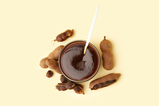 Bowl with tasty tamarind jam and fruits on yellow background