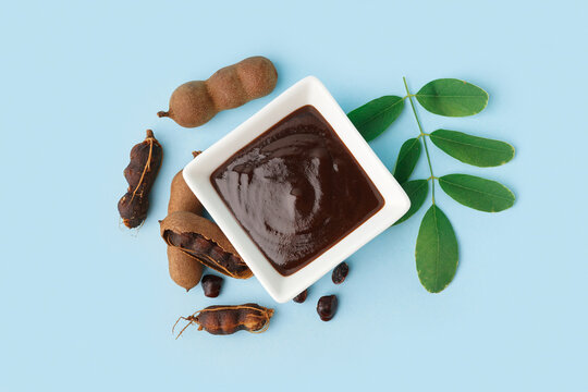 Bowl with tasty tamarind jam and fruits on blue background