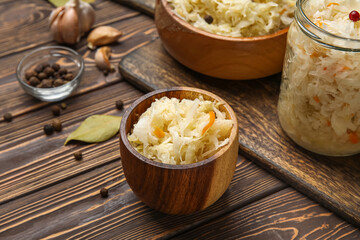 Bowl with delicious sauerkraut and different spices on wooden background