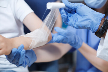 Close-up shot of a wound on the arm of a patient being carefully covered with a sterile dressing by multicultural medical professionals. Selective focus on a child being treated by a doctor and a - Powered by Adobe