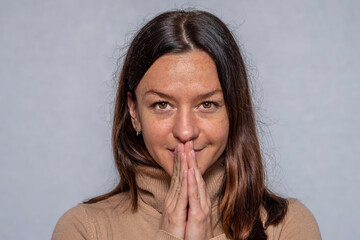 Emotional portrait of a middle-aged woman with long hair, hands folded in prayer, gray background.