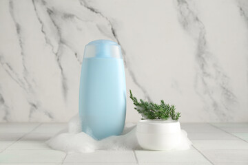 Skincare products with foam and coniferous branch on white tile table
