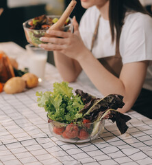 Delicious fruit and vegetables on a table and woman cooking. Housewife is cutting green cucumbers on a wooden board for making fresh salad in the kitchen.