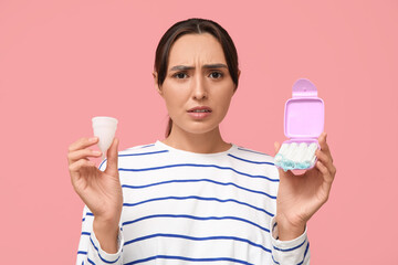 Beautiful young woman with tampons storage box and menstrual cup on pink background