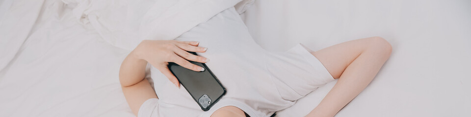 Efficient Young Millennial Girl Sitting on a Bed in the Morning, Uses Laptop Computer and Eats Croissants and Drinks Coffee for Breakfast