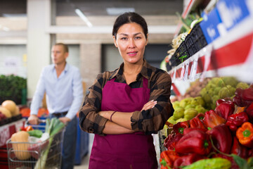 Portrait of proud confident asian saleswoman of fruit and vegetable store standing with crossed arms near counters. Successful business concept