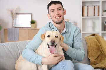 Young man with Labrador dog sitting on sofa at home