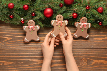 Female hands with Christmas sweet gingerbread cookies and fir branches on wooden background