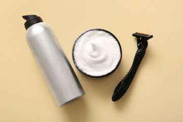Bottle of shaving foam and razor on beige background