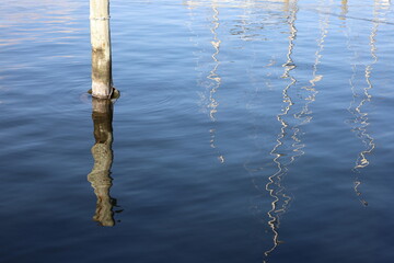 Reflection of boat masts and wooden pole in the water