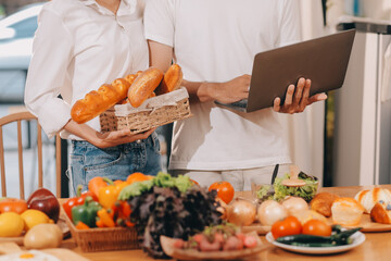 Handsome man sitting near his wife at kitchen. Family couple see social media, surf the web while sitting at kitchen table with generic laptop. Couple working with laptop at home