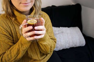 Top view of woman holding a glass mug with hot tea with lemon and honey inside, sitting on a sofa