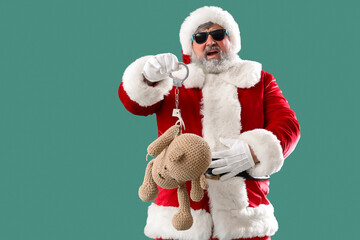 Bad Santa Claus with handcuffed toy bear on green background