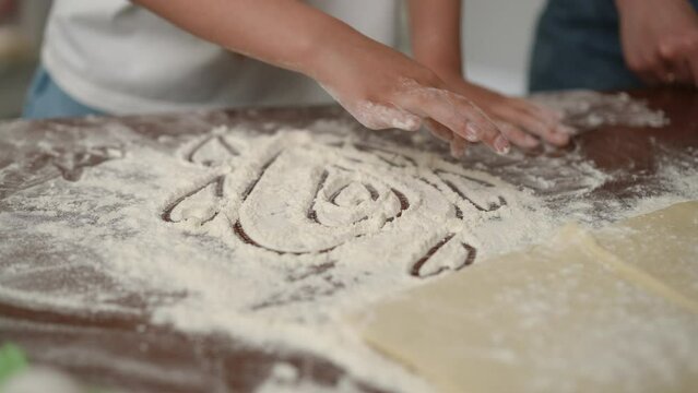 Close-up. A girl draws hearts on a table sprinkled with flour before starting to cook