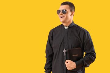 Cool priest with Holy Bible on yellow background