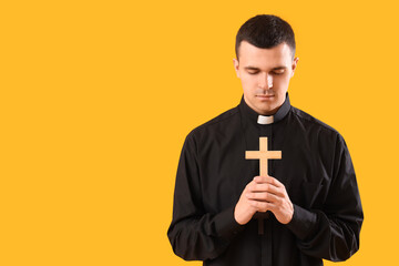 Young priest with cross on yellow background