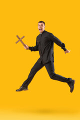 Fototapeta na wymiar Young priest with cross jumping on yellow background