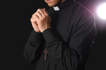Young priest praying on dark background, closeup