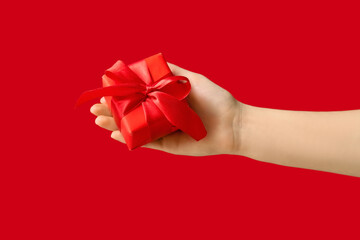 Female hand with Christmas gift box on red background