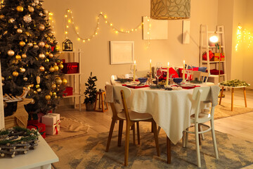 Festive table setting with burning candles and Christmas decorations in dining room at evening