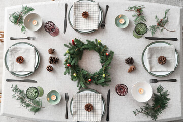 Christmas table setting with fir branches, burning candles and pine cones, top view