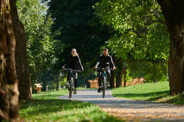 Obraz premium A blissful couple, adorned in professional cycling gear, enjoys a romantic bicycle ride through a park, surrounded by modern natural attractions, radiating love and happiness