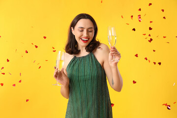 Beautiful young woman with glasses of champagne on yellow background