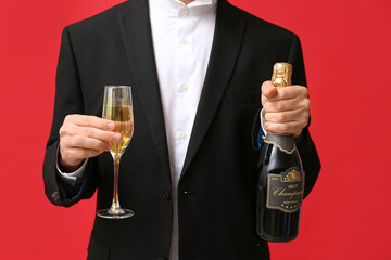 Young man with glass and bottle of champagne celebrating Christmas on red background