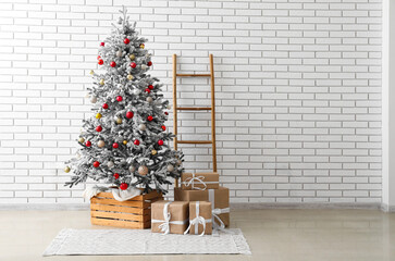 Beautiful Christmas tree, gift boxes and ladder near light brick wall