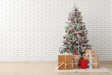 Decorated fir tree and different presents near light brick wall