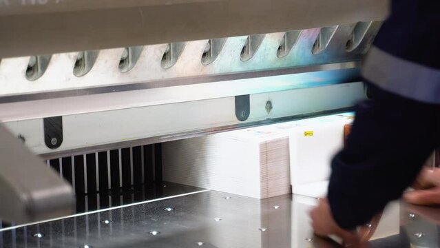 Worker cutting paper using paper cutting machine in a printing factory