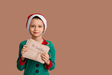 Cute little boy in Christmas pajamas with gift on brown background